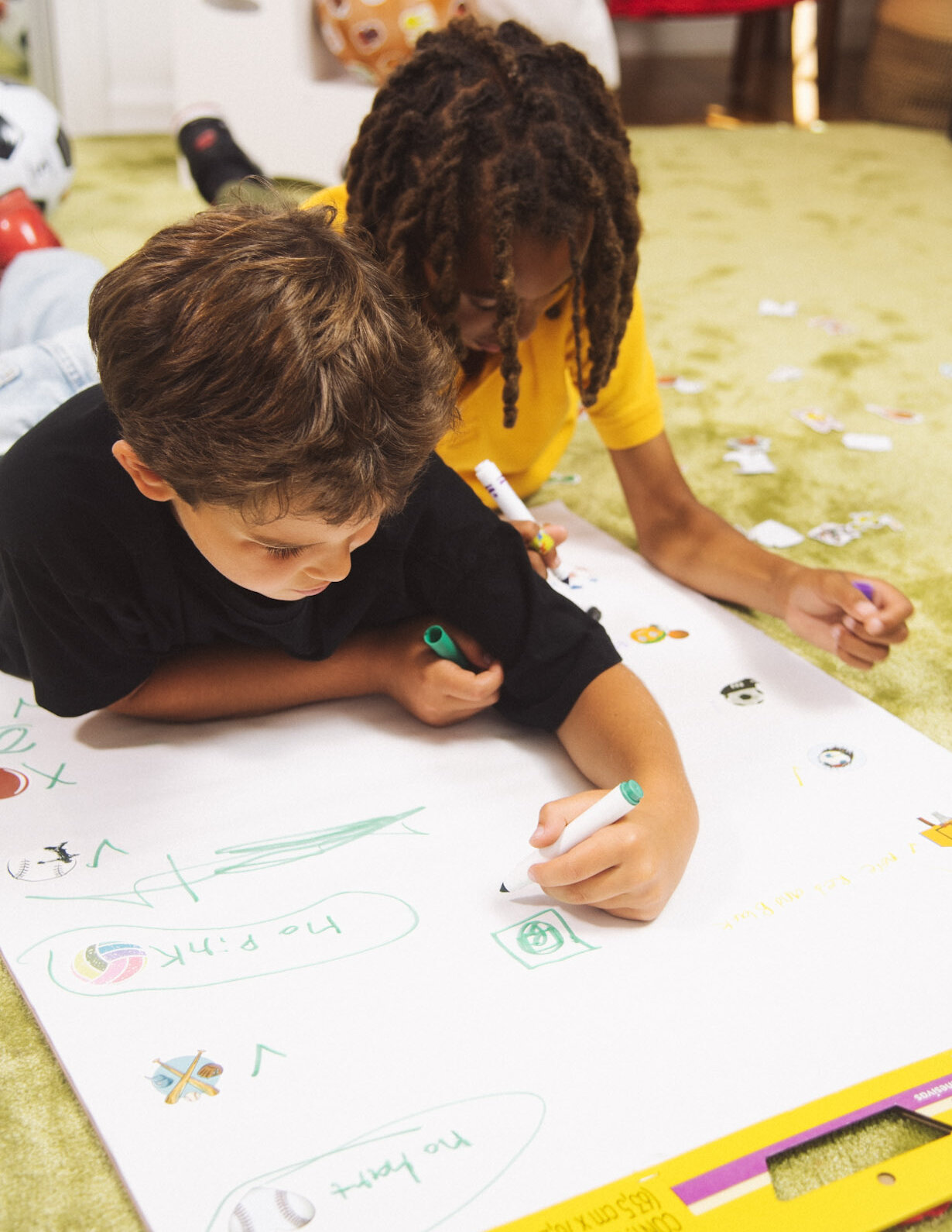 Two boys sprawled on the rug working on a poster together, markers out